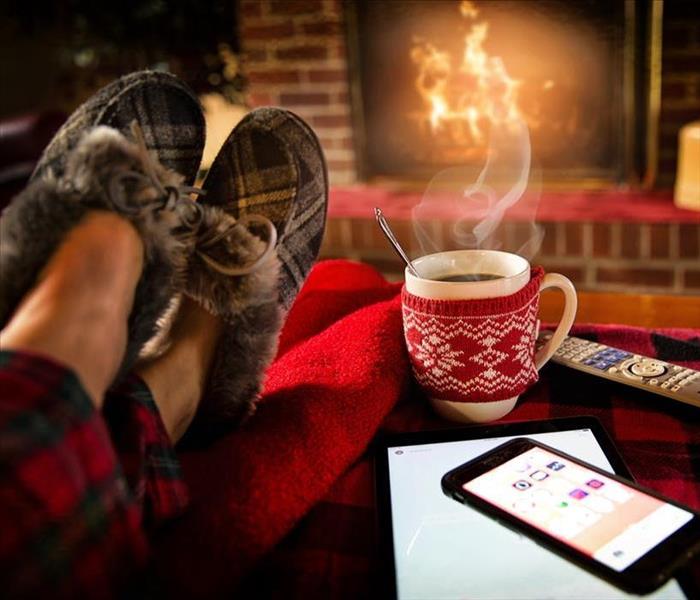 A person relaxing by a fire with a hot drink in hand